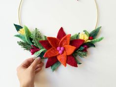 This handmade Christmas wreath, adorned with a festive bow and vibrant poinsettias, adds a touch of luxury to your holiday decor. Crafted from high-quality felt, this custom wreath is perfect for decorating your front door or enhancing your indoor space. Ideal for those seeking a unique Christmas gift or a luxurious holiday decoration, this wreath will elevate any winter wonderland setting. Its elegant design makes it the perfect addition to your festive celebrations. ✿ DETAILS ✿ - Hand-felted with love by artist Adelya Tumasyeva using high-quality merino wool. Each wreath design is unique. - Each leaf and petal is made from loose sheep hair using and needle-felting technique. It takes ~10 hours to make.  - Felt wreaths are extremely durable, they do not fade, and will look beautiful for y Felt Poinsettia Wreath, Felt Christmas Wreath, Felt Poinsettia, Felt Wreaths, Wreath Unique, Holiday Door Decor, Wreath With Bow, Handmade Christmas Wreaths, Custom Wreath