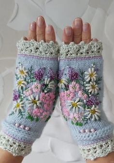 a woman's hand is holding up a pair of knitted gloves with flowers on them