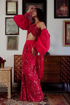 Step into iconic glamour where elegance is draped in the shimmer of scarlet palette for the season’s soirees. Our new-age concept of pre-draped saree features a chic halter neck blouse adorned with nalki crystals embellishment paired up with a sequined pre-draped skirt. Adding a hint of drama the handmade puffer sleeves complete the whole iconic look. • Pre-draped sequined skirt.• Halter-neck blouse adorned with nalki crystals and moti embellishments. • Metal hook at the back side of the blouse to conceal. • Puffed sleeves with an attached sequined dupatta.• Metal zip on the backside of the skirt along with a hook for support.From Moledro’s Fitoor collection. DELIVERY TIMEPlease allow 8-12 weeks for your outfit to arrive. FABRIC DETAILSBlouse: Butterfly Net Skirt: GeorgetteSleeves: Net Pro Skirt Drape, Skirt Saree, Halter Neck Blouse, Net Sleeves, Sequined Skirt, Halter Neck Blouses, Georgette Skirt, Net Skirt, Draped Saree