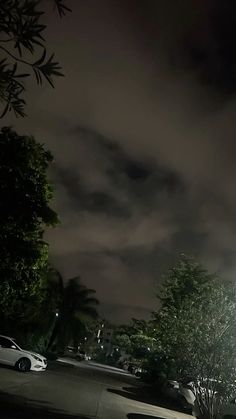 cars parked in a parking lot at night with the lights on and dark clouds overhead