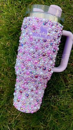 a purple and white cup with lots of beads on it sitting in the green grass