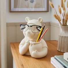 a ceramic bear with glasses and pencils on a table in front of a vase