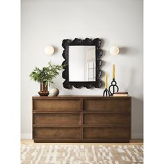 a large mirror on the wall above a dresser with plants and vases in front of it