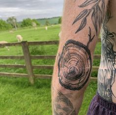 a man with tattoos on his arm standing in front of a fence and sheep grazing