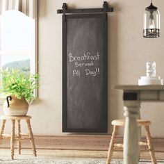 there is a chalkboard on the wall next to two stools and a potted plant