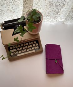 an old typewriter sitting next to a potted plant on top of a table