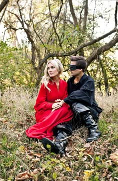 a man and woman sitting on the ground next to each other in front of trees