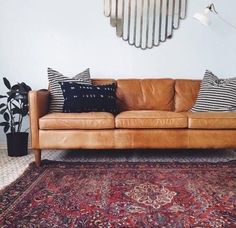 a brown leather couch sitting on top of a rug in front of a white wall