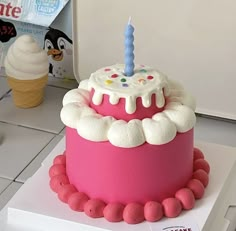 a pink birthday cake sitting on top of a white counter next to an ice cream cone