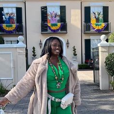 a woman standing in front of a house with her arms out and holding a handbag