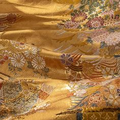 an image of gold fabric with flowers and leaves on it's side, close up