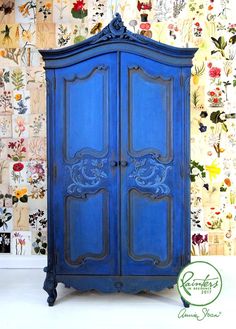 an ornate blue armoire against a floral wallpaper