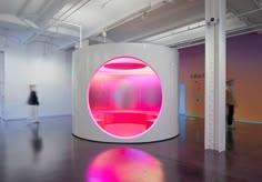 a large round white object with pink lights in an office space, surrounded by people