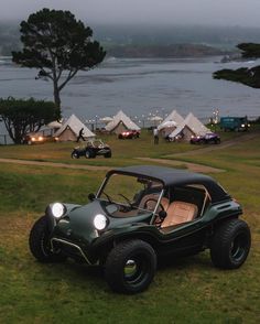 an old style buggy is parked on the grass near some tents and water in the background