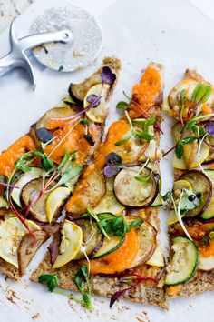 a pizza topped with veggies and sauce on top of a white plate next to a fork