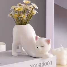 a white cat figurine sitting on top of a book with flowers in it