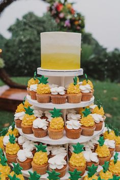 a three tiered cake with pineapples on top and cupcakes below