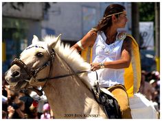 a woman riding on the back of a brown and white horse in front of a crowd