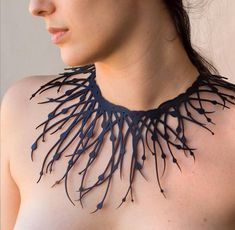 a woman with very large breast wearing a necklace made out of black plastic branches on her chest