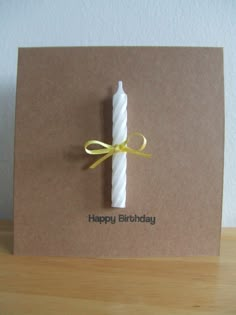 a brown card with a white candle on it and a yellow ribbon around the edge