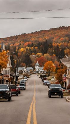 cars are parked on the street in front of houses with autumn trees lining the road