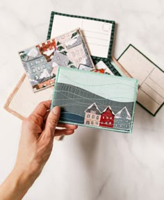 someone is holding a small card case in front of some postcards and envelopes