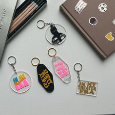 several keychains with different designs on them sitting next to some pens and pencils