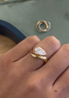 a woman's hand holding a diamond ring on top of a table with other jewelry