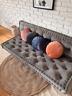 a gray couch with four pillows on it in front of a brick wall and rug