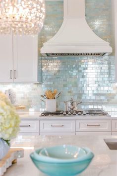 a white kitchen with blue glass backsplash and chandelier over the stove