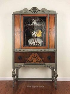 an old china cabinet with glass doors and flowers in the top drawer, on a wooden floor