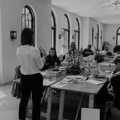 a group of people sitting around a wooden table in a room with arched windows on the walls