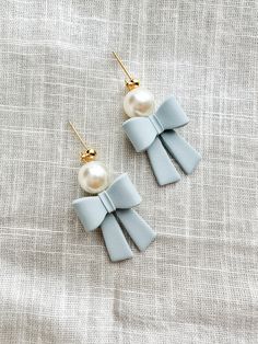 two pairs of earrings with bows and pearls on top of a gray fabric background,