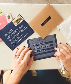 two hands holding a piece of paper next to some envelopes and other items on a table