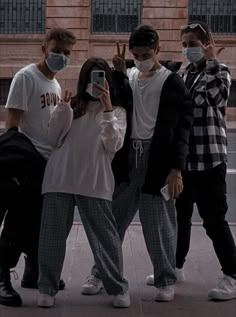 four people wearing face masks taking a selfie in front of a brick building with their cell phones