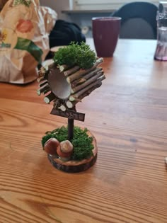 a small tree made out of sticks and moss on top of a wooden table next to a phone