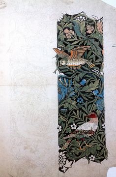 an old wall hanging with birds and flowers on it's side, next to a plant