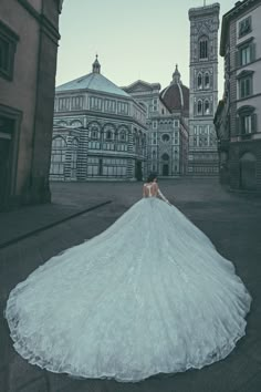 a woman in a white wedding dress is standing on the street with buildings behind her