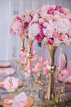 a table topped with lots of pink flowers next to tall vases filled with candles