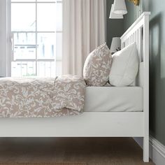 a white bed sitting in a bedroom next to a window with curtains on the windowsill