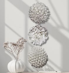 three white vases with flowers in them sitting on a table next to a wall