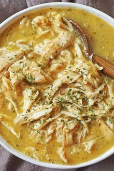 a white bowl filled with chicken and noodles next to a wooden spoon on top of a table