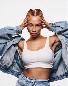 a woman in white top and jean jacket holding her hands to her head with both hands