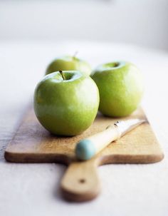 two green apples sitting on top of a cutting board