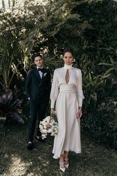 a man and woman standing next to each other in front of some bushes with flowers