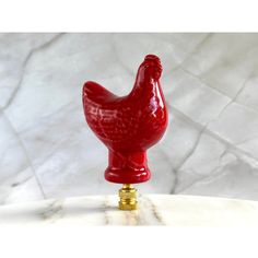 a red rooster figurine sitting on top of a marble table