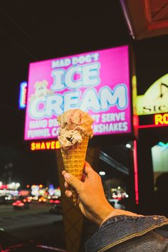 a hand holding an ice cream cone in front of neon signs