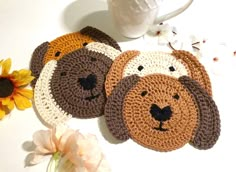 three crocheted coasters with dogs on them next to a cup and flower