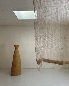 a tall vase sitting next to a window in a room with a curtain hanging from the ceiling