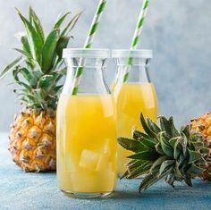 pineapple juice in glass bottles next to sliced pineapples on blue tablecloth